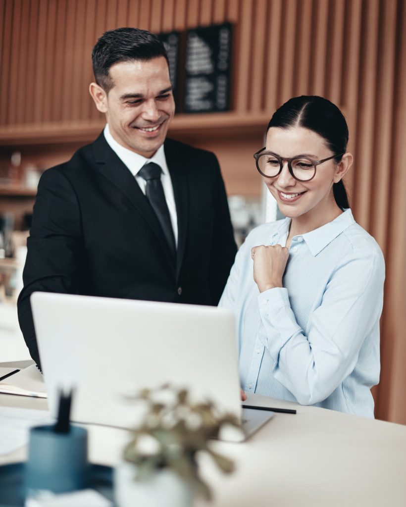 Two smiling businesspeople using a laptop together in an office